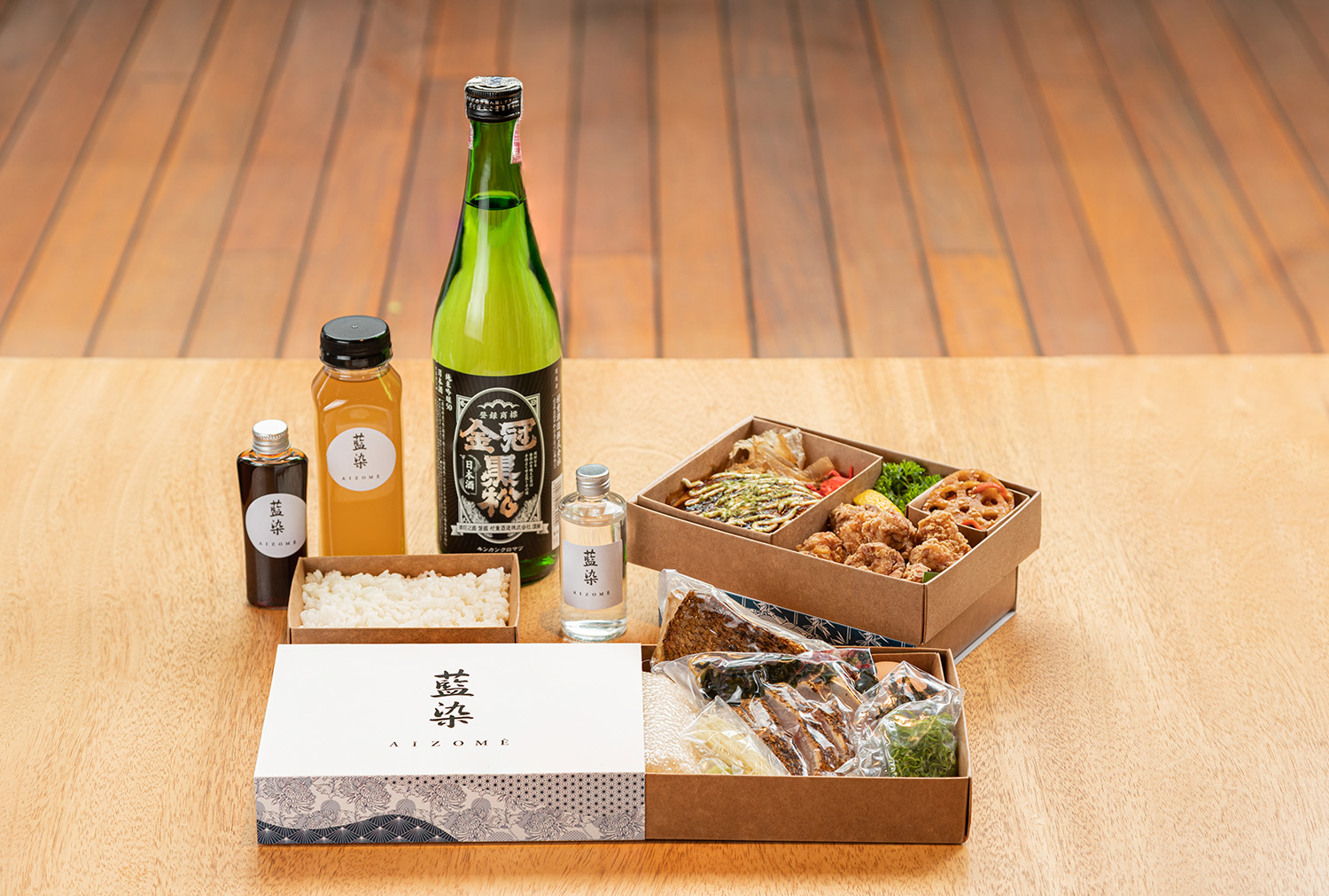 Kit gastronômico da Experiência JHSP: Cultura e Gastronomia de Setouchi Oeste. Garrafas de diferentes tamanhos e caixas de comidas sobre mesa de madeira clara. 
