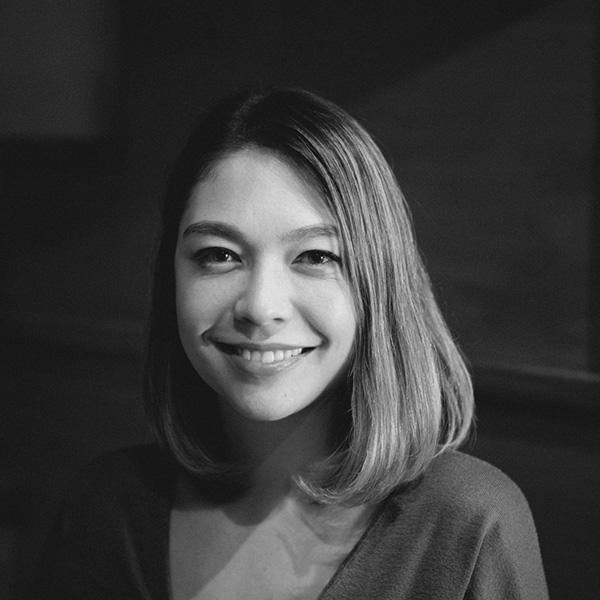 Fotografia em preto e branco de Tina Koyama. Tina é uma jovem com traços asiáticos, cabelos lisos na altura do ombro com reflexos em cor loira. 